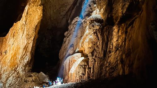 Escursionisti ascoltano la guida sotto il fascio di luce all'interno della grotta Sa Nurre de Su Hoda a Oliena