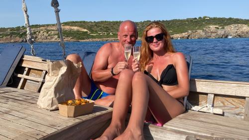 Ein Paar prostet sich mit Weißwein bei einem Ausflug ins Meer von Alghero zu