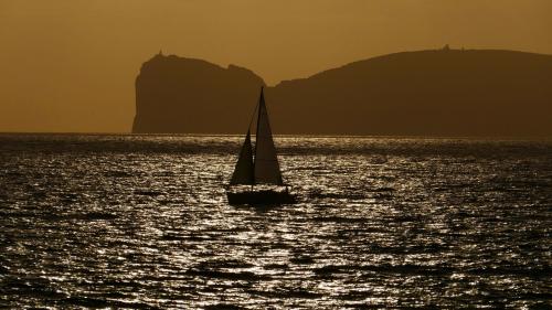 A sailing boat at sunset in the waters of Alghero