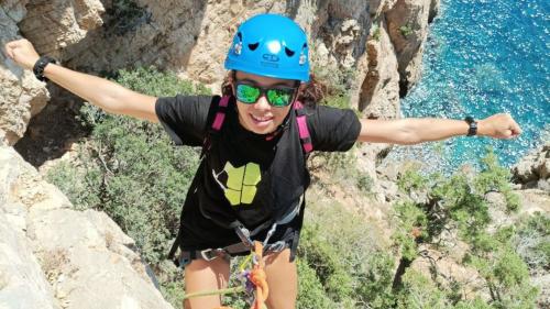 Girl during rope abseil with equipment and sea of Orosei