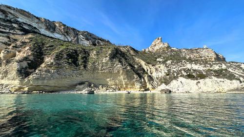 Mer turquoise pour nager et faire du snorkeling dans le Golfo degli Angeli avec du sable blanc et fin et de hautes falaises surplombant la mer.