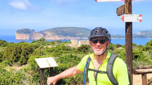 Junge mit Helm und E-Bike erkundet Alghero mit Capo Caccia im Rücken