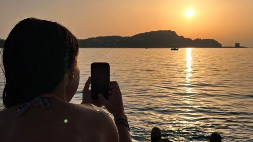 A girl takes a photo of the sunset at La Pelosa
