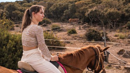 Girl admires the landscape while riding a horse in Sedini